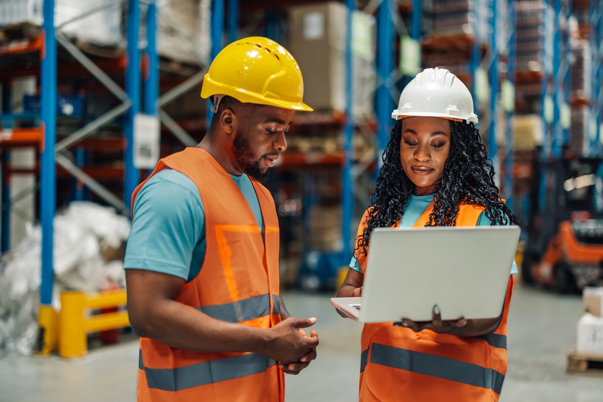Two,Warehouse,Workers,Are,Holding,A,Laptop,And,Discussing,About